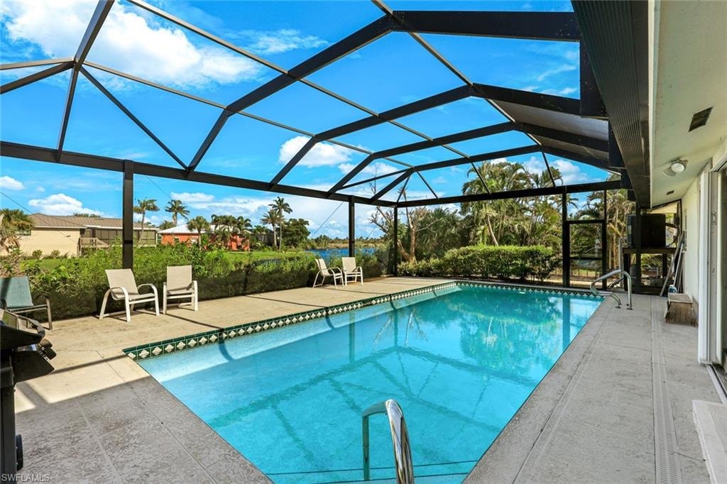 Resort-style screened pool enclosure featuring a sparkling blue saltwater pool with geometric tile accents, expansive concrete decking, and a sophisticated black aluminum frame structure