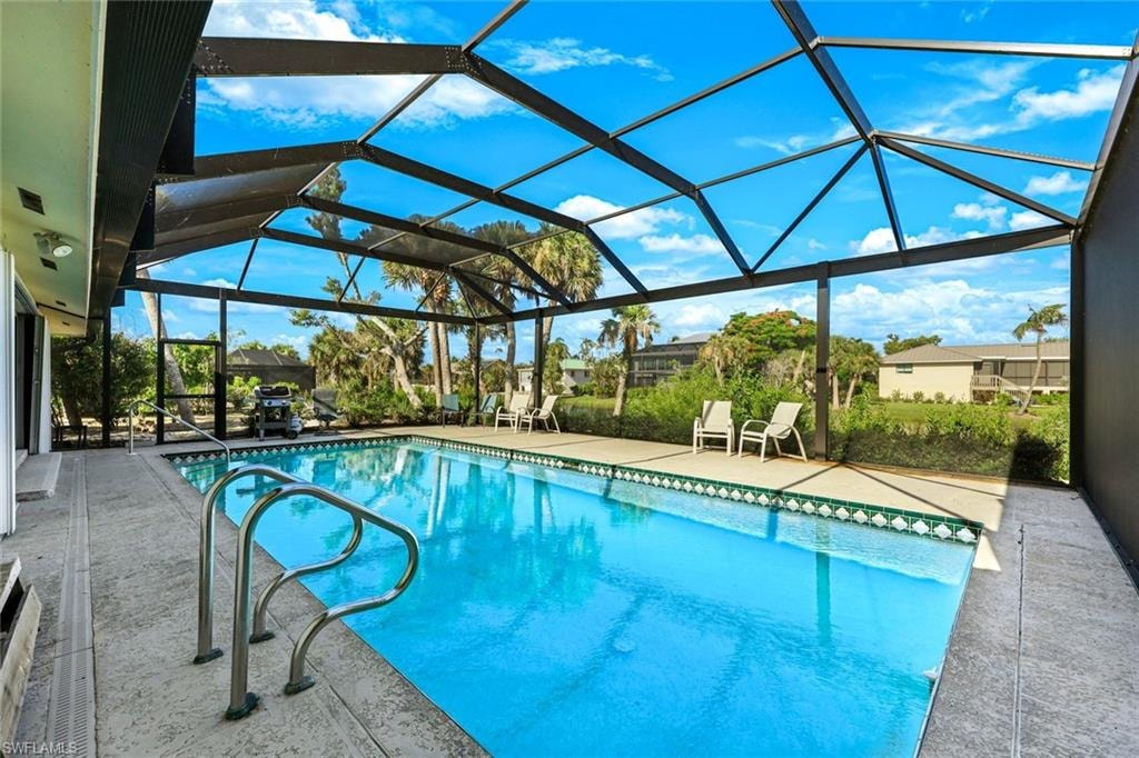 Screen-enclosed pool featuring a textured concrete deck, integrated pool steps with handrails, and a decorative tile border