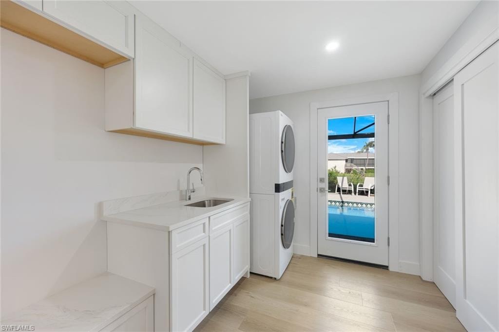 Dedicated laundry room featuring white cabinetry with ample storage, stainless steel front-load washer and dryer unit, quartz countertop with integrated sink, wood-finish floating shelving, and direct access to outdoor spaces through glass door with natural light throughout