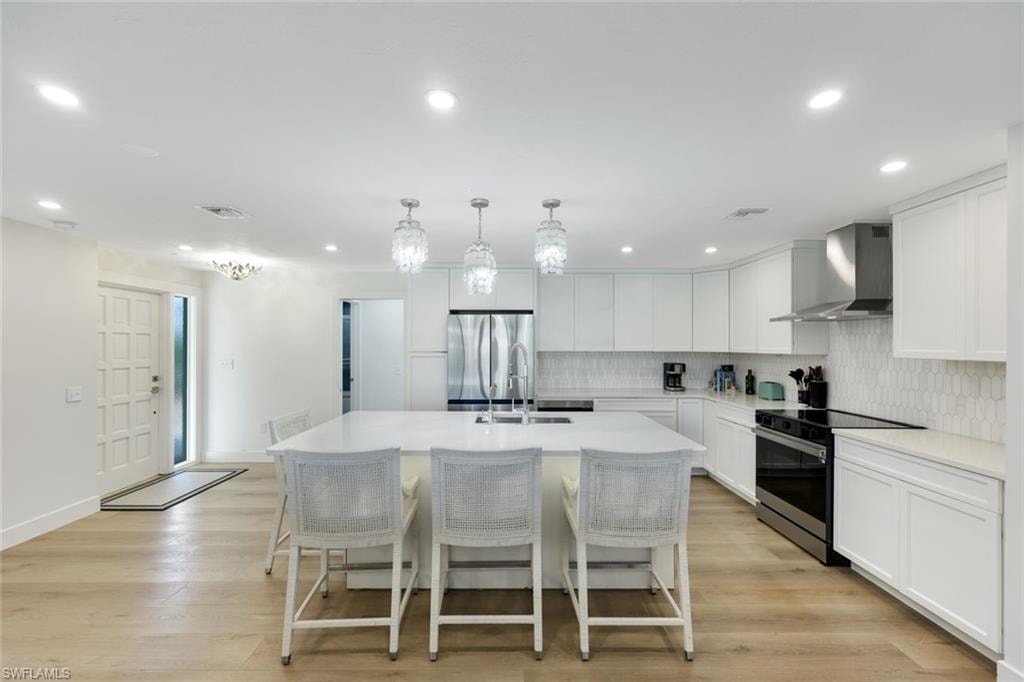 Open-concept kitchen featuring a large island, white cabinetry, integrated stainless steel appliances, a tiled backsplash, and recessed lighting