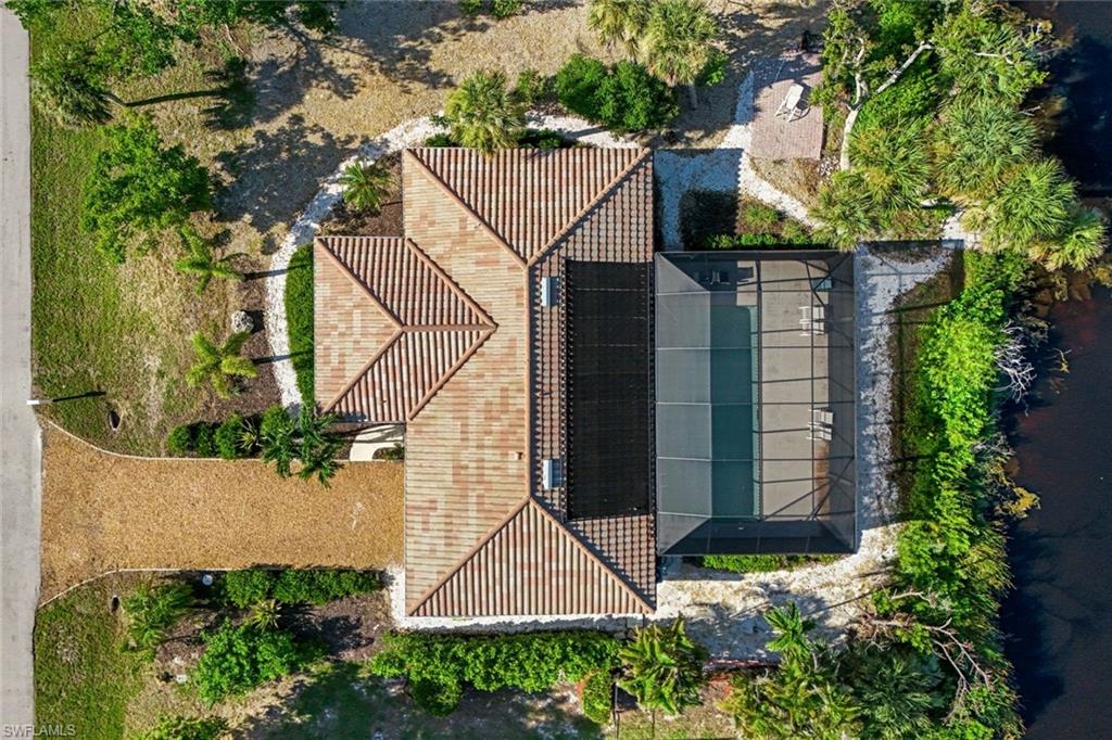 Tile roof home featuring a screened-in pool enclosure, gravel driveway, and mature landscaping
