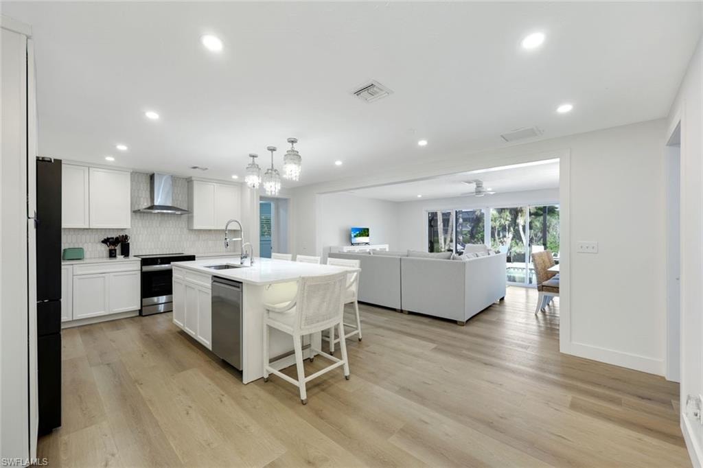 Bright kitchen featuring white cabinetry, a large center island with seating, stainless steel appliances, and wood-finish flooring