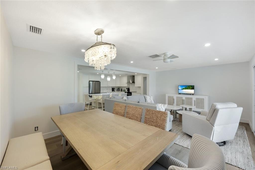 Open-concept dining and kitchen area featuring a light wood-finish dining table, crystal chandelier with brushed metal finish, stainless steel appliances, white cabinetry, and recessed ceiling lighting
