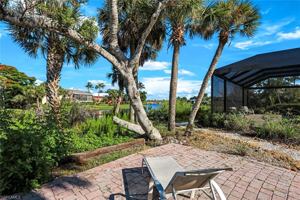 Brick paver patio with lush tropical landscaping and mature palm trees, featuring a screened enclosure and water views