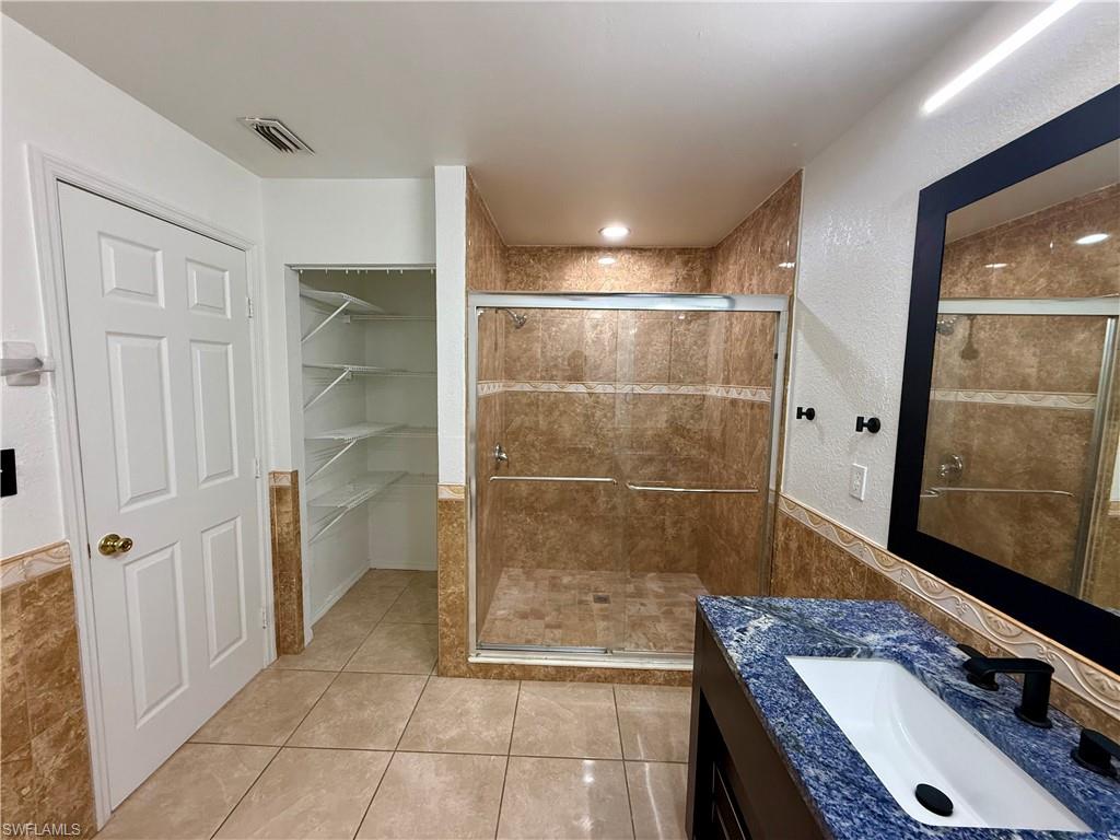 Bathroom featuring a tiled shower with glass enclosure, a vanity with a blue granite countertop and undermount sink, and tiled flooring