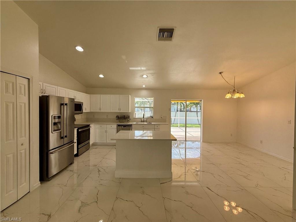 Open-concept kitchen and living area featuring white cabinetry, stainless steel appliances, a center island, vaulted ceilings, and large format tile flooring