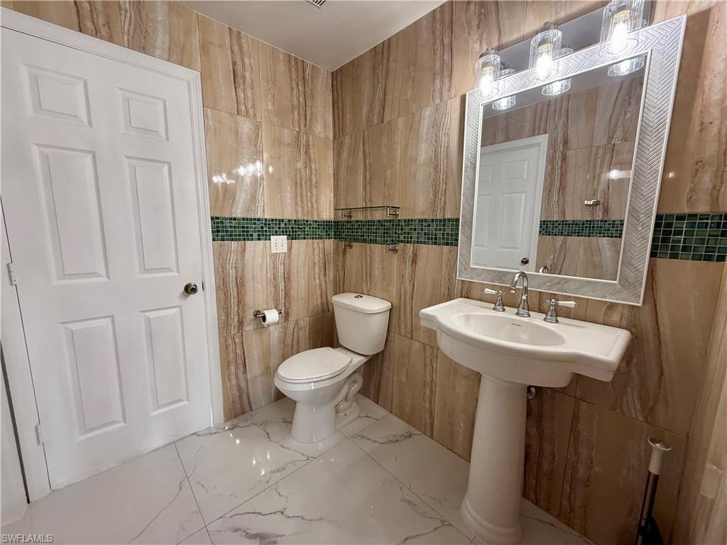 Bathroom featuring floor-to-ceiling stone-look tile, a green mosaic tile accent band, and white porcelain pedestal sink