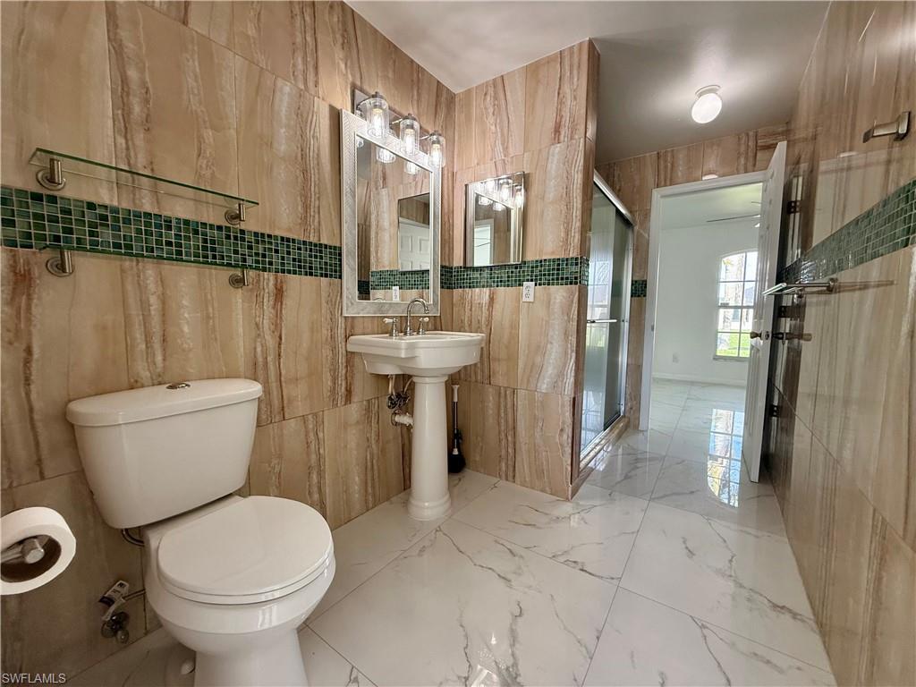 Bathroom featuring full-height stone-look wall tiling with a mosaic accent band, white pedestal sink, and a glass-enclosed shower