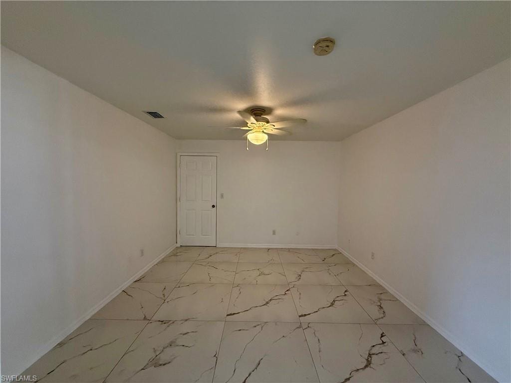 Spacious room featuring large format tile flooring with distinctive veining, a ceiling fan with integrated lighting, and a paneled interior door