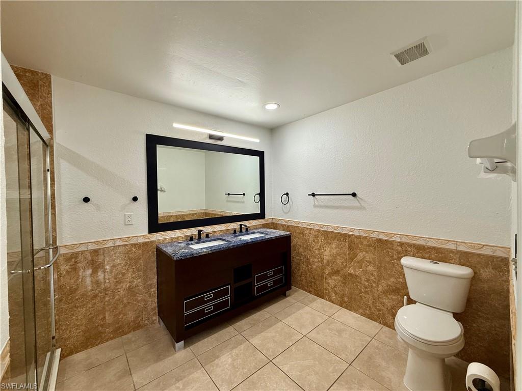 Spa-inspired master bathroom featuring a dual-sink vanity with wood cabinetry, ceramic tile flooring, and a large framed mirror with integrated lighting