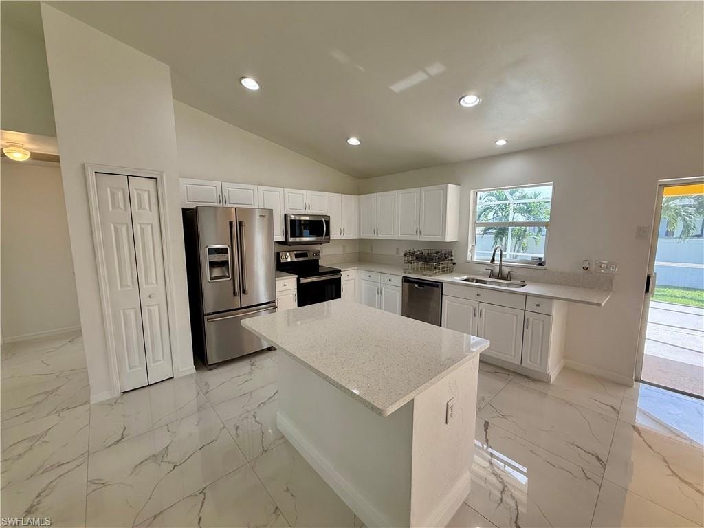 Bright kitchen featuring a central island, white cabinetry, stainless steel appliances, recessed lighting, and large format marble-look tile flooring