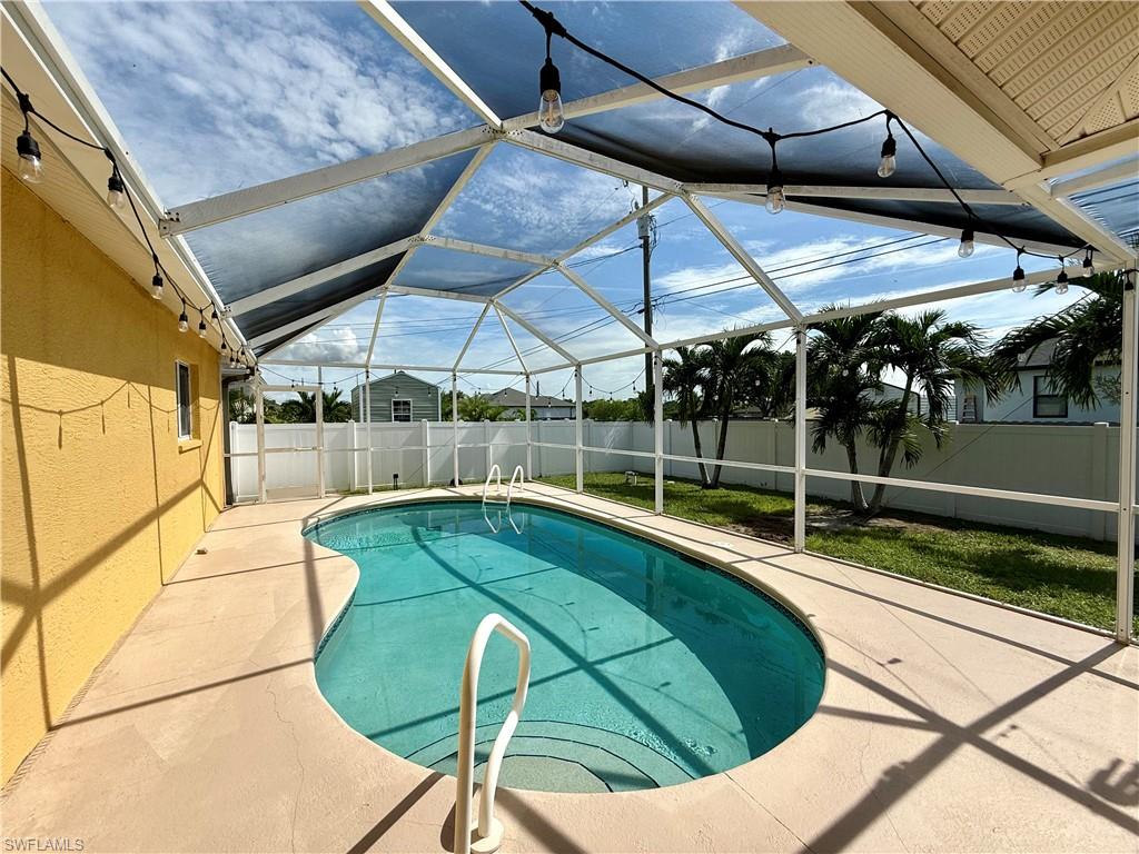 Screened pool enclosure featuring a resort-style kidney-shaped pool with turquoise water, white safety railings, and expansive concrete decking