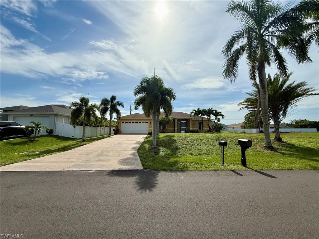 Single-story residence featuring a two-car garage, mature palm trees, and a spacious front lawn
