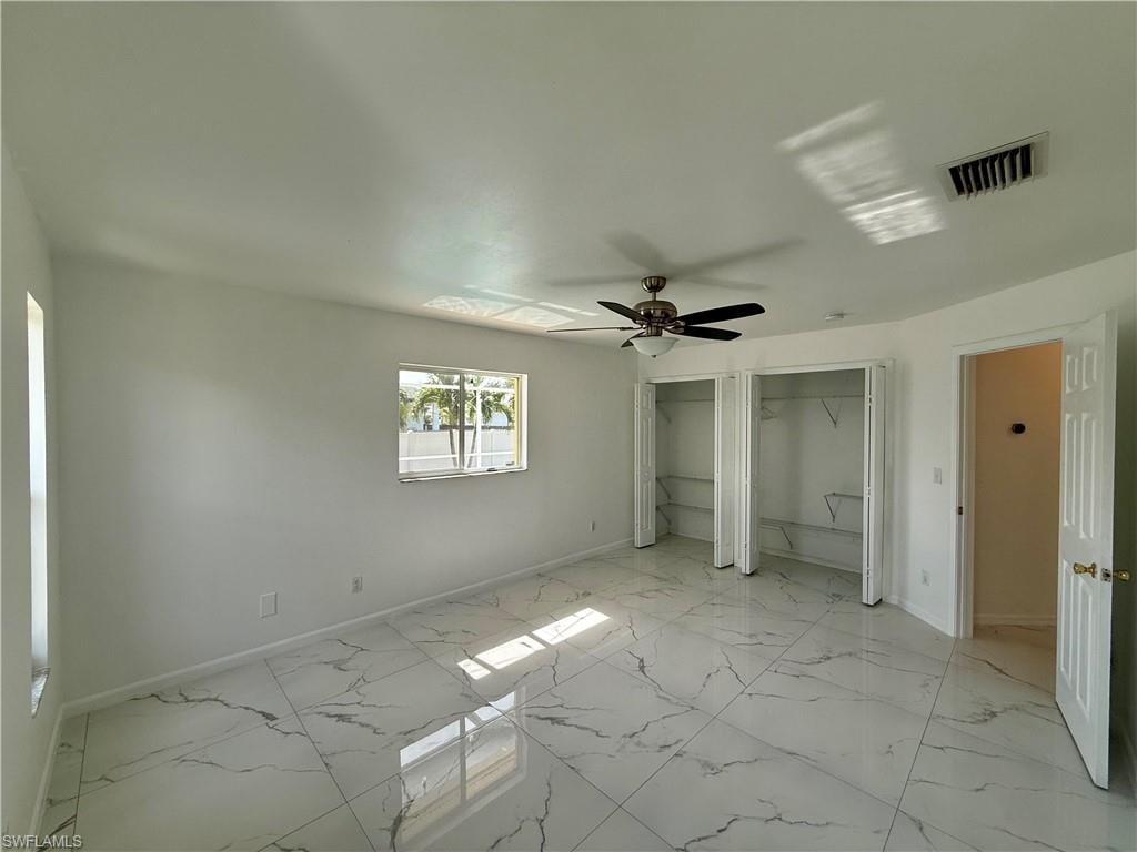 Spacious interior featuring white walls, large format tile flooring with veining, and a ceiling fan with integrated lighting