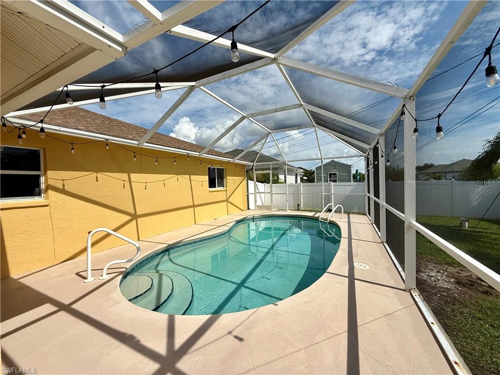 Screened-in pool with a light-colored paved deck and string lighting