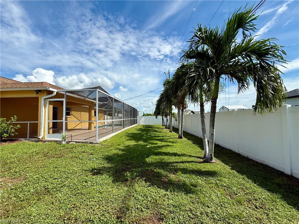 Spacious backyard oasis featuring mature palm trees, manicured lawn, and a screened enclosure with wood-finish exterior