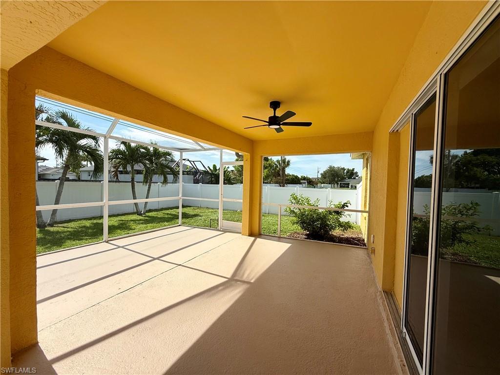 Expansive screened patio featuring a ceiling fan, concrete flooring, and direct access to a private backyard with a white privacy fence and mature palm trees