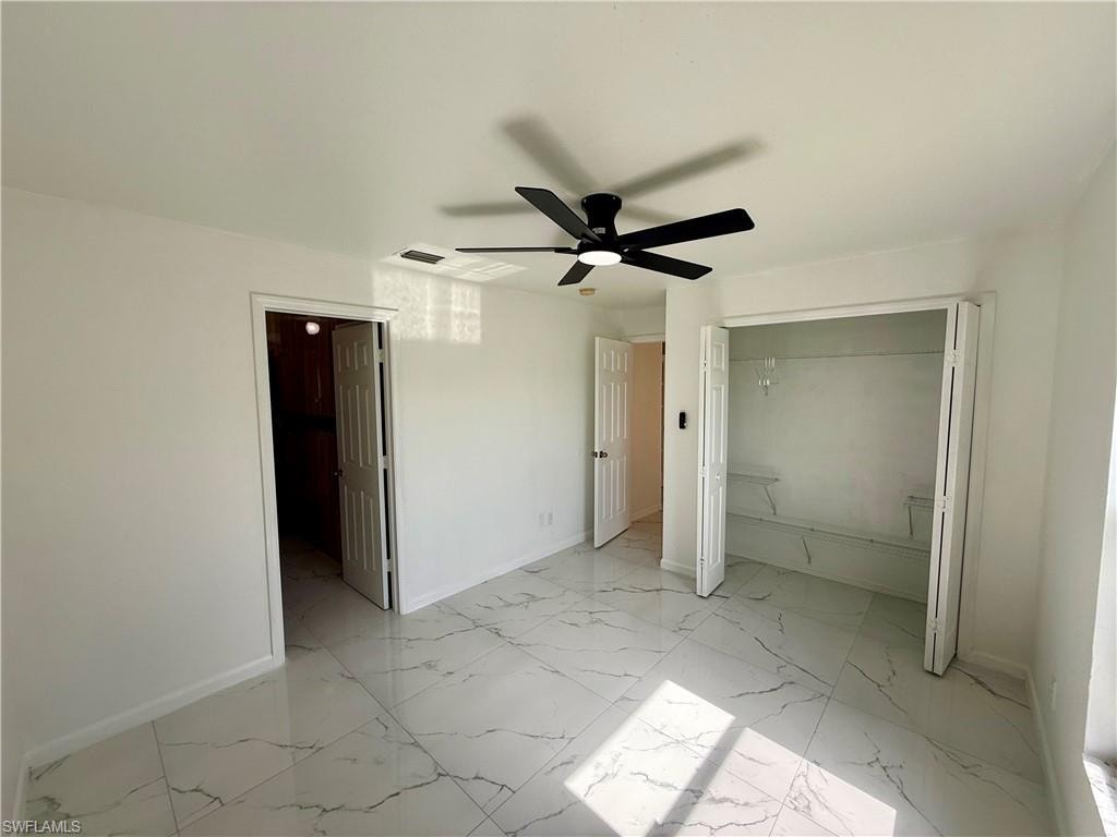 Spacious room featuring large format white tile flooring with gray veining, a ceiling fan with integrated lighting, a double-door closet with shelving, and crisp white walls