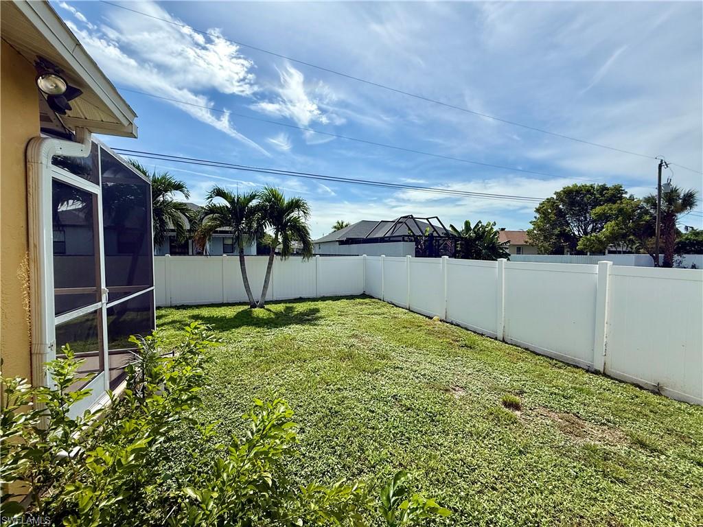 Expansive backyard featuring a manicured lawn, established palm trees, and a full privacy fence