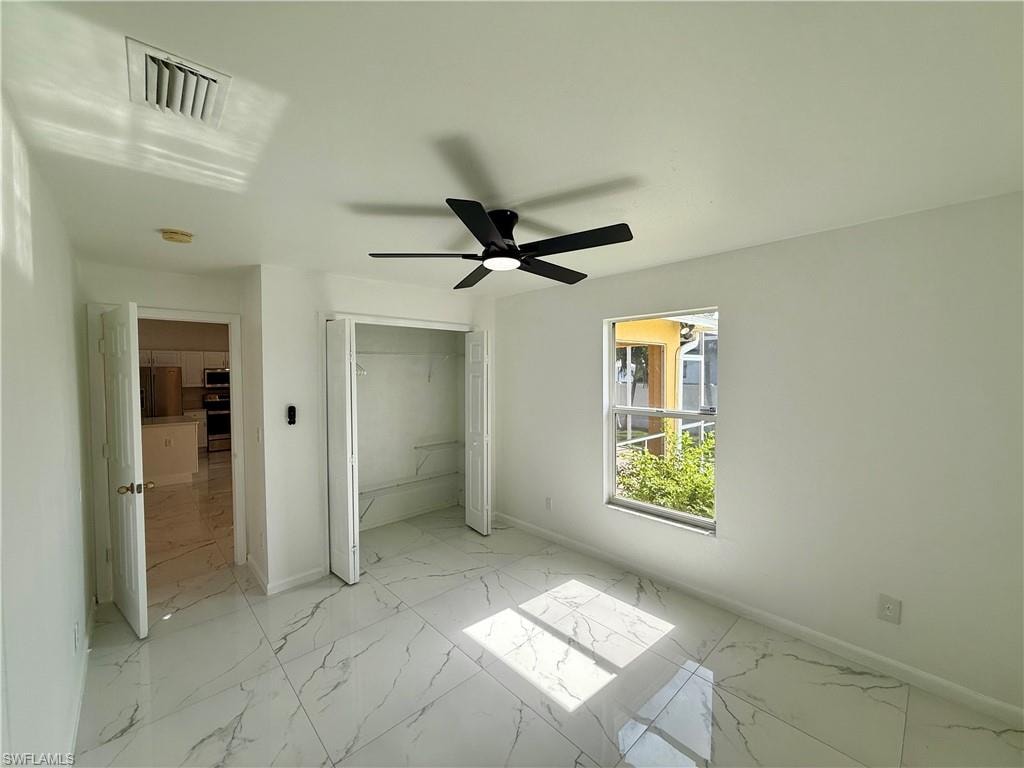 Spacious room featuring large format tile flooring, a window with exterior visibility, a ceiling fan with integrated lighting, and a bi-fold closet