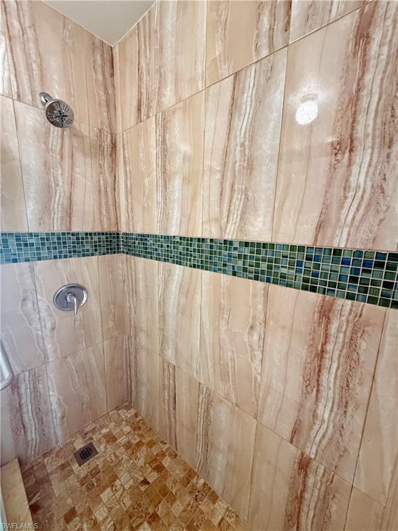 Shower featuring vertical-format stone-look wall tiles, a mosaic tile accent band, a square-tile shower floor, and a chrome showerhead with matching controls