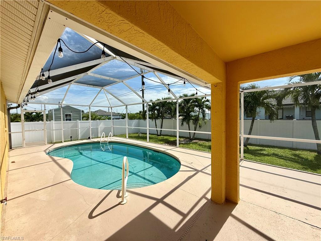 Screened-in pool area featuring a freeform pool with a ladder, a concrete pool deck, and string lighting