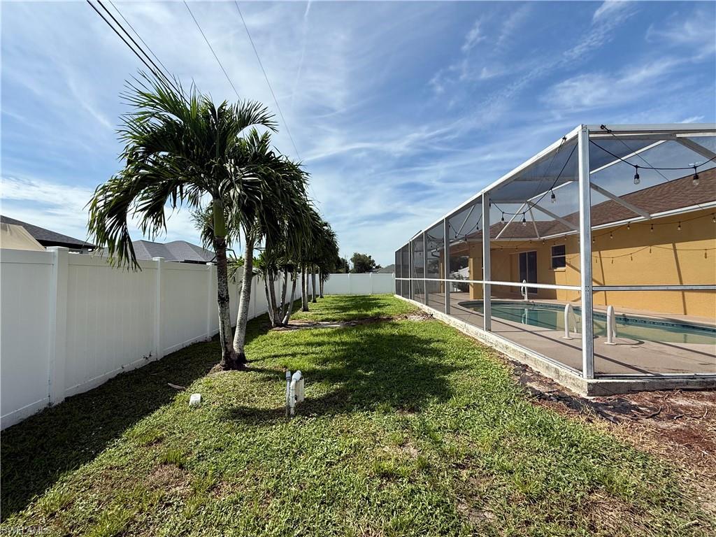 Expansive backyard featuring a mature palm tree, lush manicured lawn, and white vinyl fencing along the perimeter