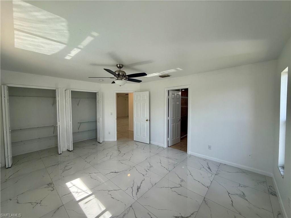 Spacious room featuring large format white tile flooring with gray veining, dual bi-fold door closets, a ceiling fan with integrated lighting, and multiple entryways