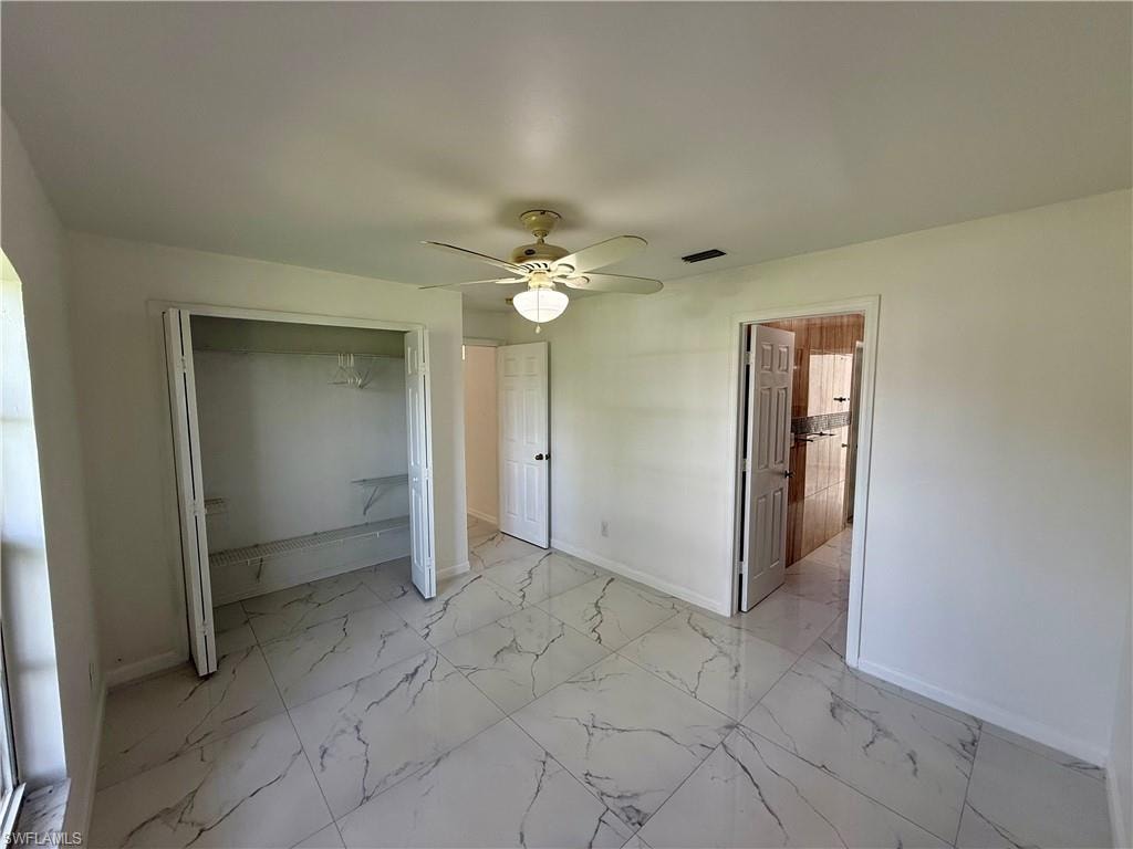 White interior featuring large format marble-look tile flooring, a ceiling fan with integrated lighting, a bifold closet with shelving, and a white interior door
