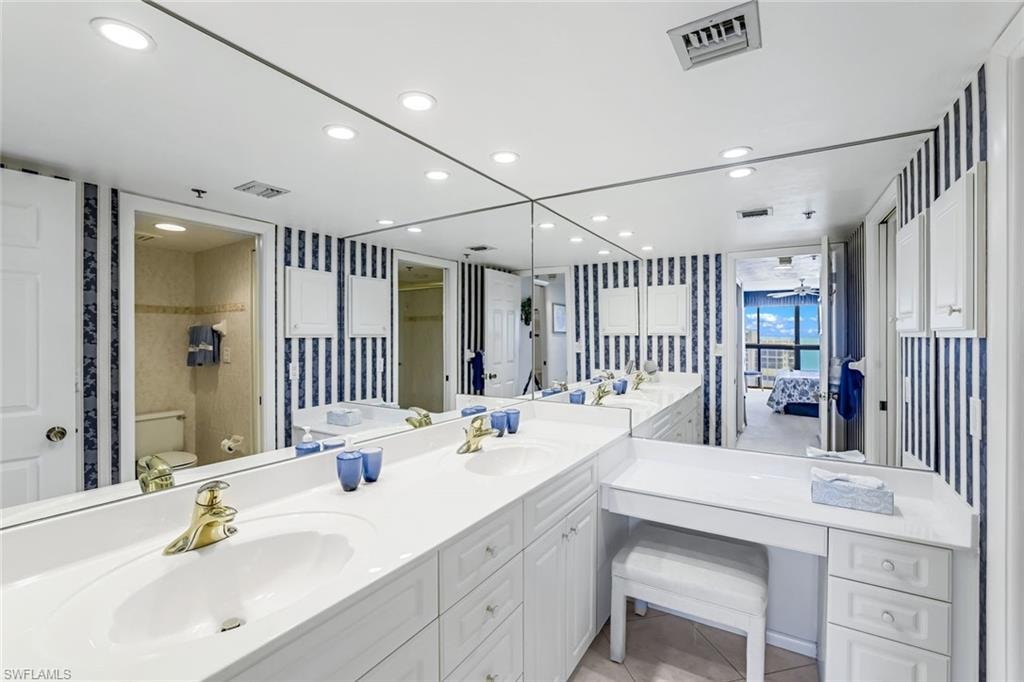 Spacious bathroom featuring a dual vanity with gold-tone fixtures, full-wall mirror, built-in makeup vanity, recessed lighting, and ample storage cabinetry