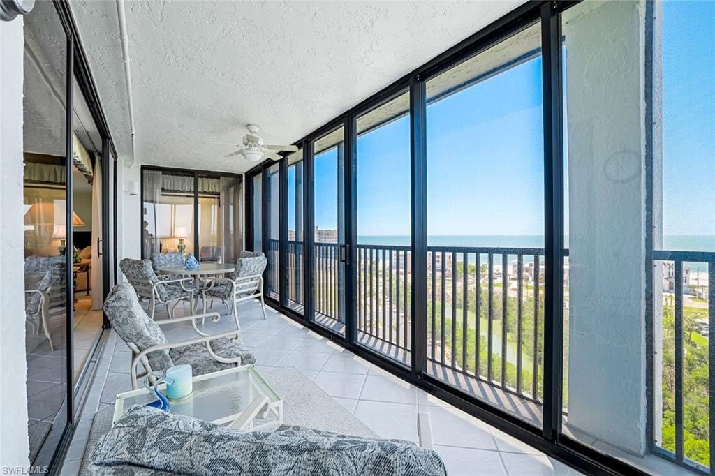 Screened balcony featuring full-height glass panels, white tile flooring, a textured ceiling, and a ceiling fan