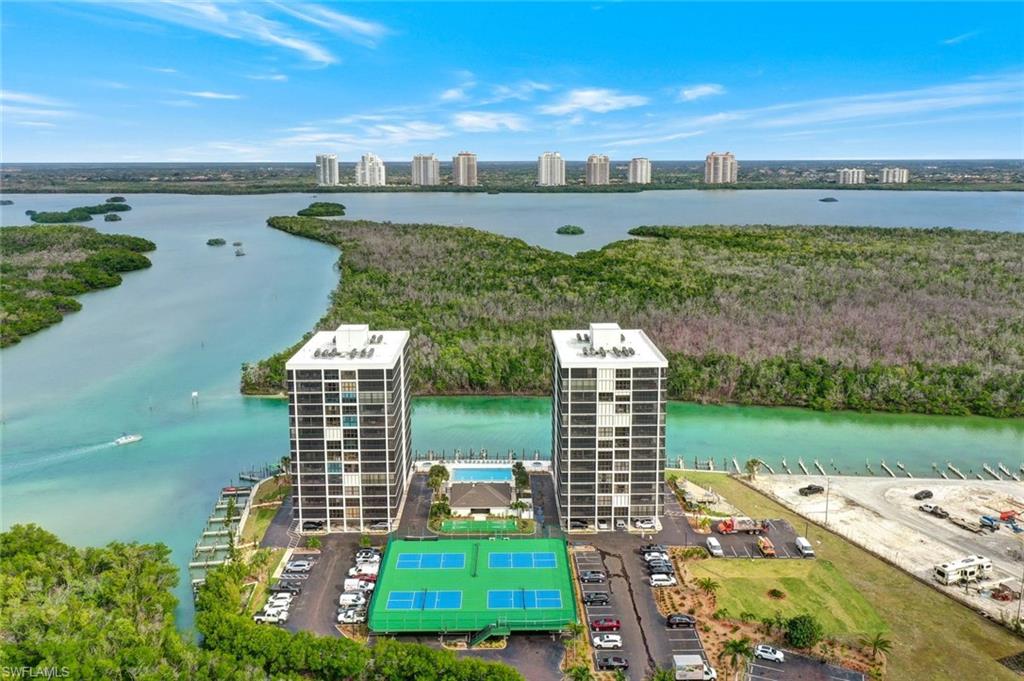 Twin high-rise residential buildings featuring private balconies, waterfront access, a tennis court, and a central swimming pool with an accompanying clubhouse