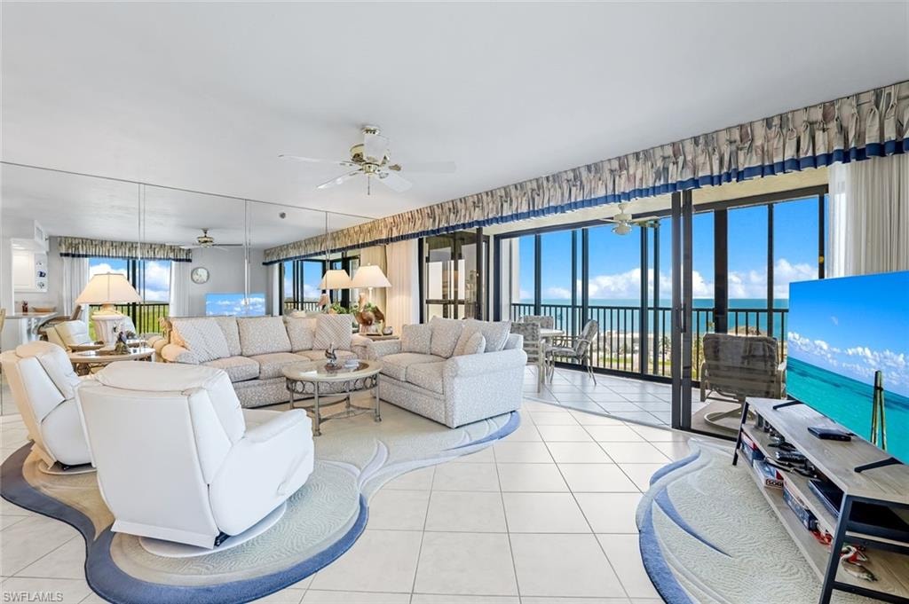 Expansive living area featuring floor-to-ceiling sliding glass doors, tile flooring, a mirrored accent wall, and ceiling fan