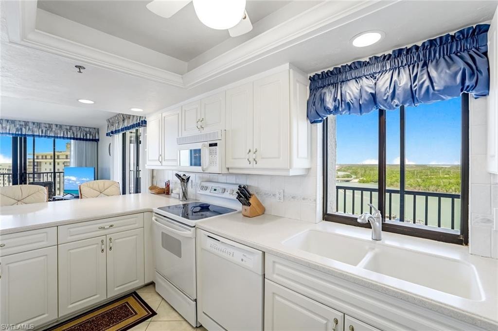 Kitchen featuring white cabinetry with brushed nickel hardware, a dual basin sink, white appliances, and a window with water and tree scenery
