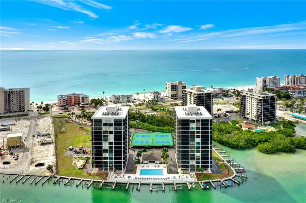 Waterfront high-rise community featuring multiple residential buildings, private boat docks, a tennis court, and an outdoor swimming pool with surrounding lounge areas