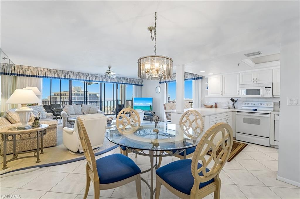 Open-concept living space featuring a full wall of floor-to-ceiling windows, white tile flooring, a dining area with a glass-top table, and a kitchen with white cabinetry and appliances