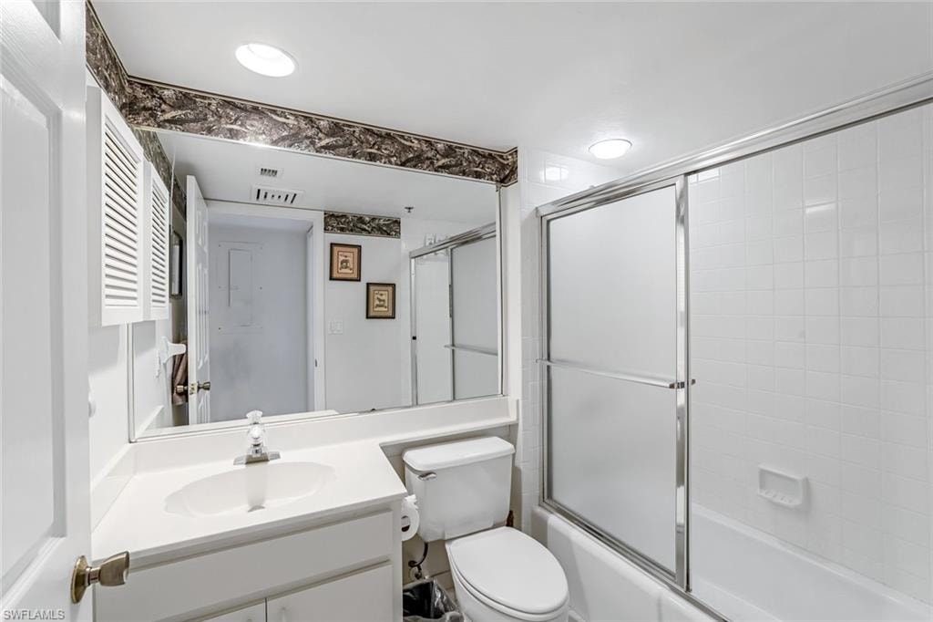 Full bathroom featuring a white vanity with integrated sink, a large mirror, and a combination shower-tub with sliding frosted glass doors