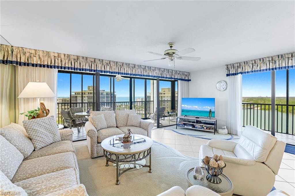 Expansive high-rise living room featuring floor-to-ceiling sliding glass doors, panoramic oceanfront vistas, neutral tile flooring, and layered window treatments with coordinating drapery