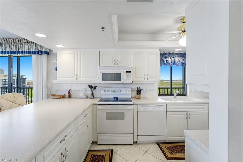 Bright kitchen featuring white cabinetry, a white appliance suite, and a large countertop peninsula