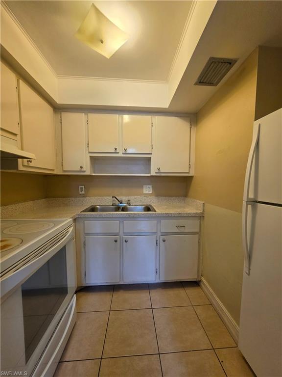 Compact kitchen featuring a double basin stainless steel sink, white cabinetry, light-toned countertops, and square tile flooring