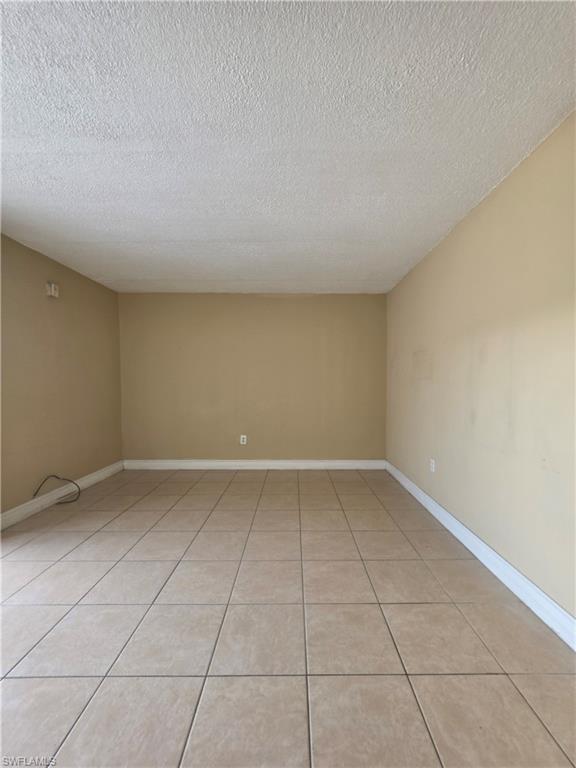 Spacious room featuring neutral-toned walls, a textured ceiling, and large square tile flooring