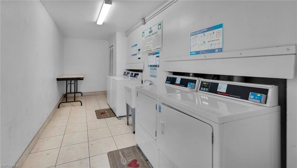 Dedicated laundry room featuring side-by-side washer and dryer units with digital controls, tile flooring, fluorescent ceiling lighting, and informational signage on the walls