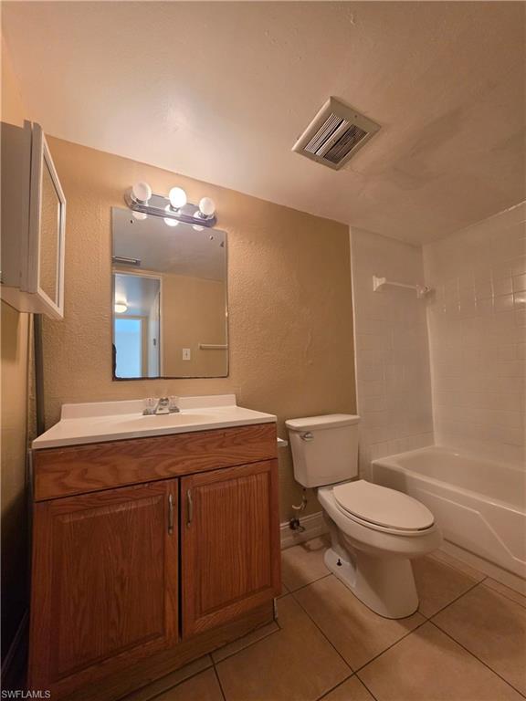 Bathroom featuring a wood-finish vanity with an integrated sink and countertop, a wall-mounted mirror with overhead lighting, a white toilet, and a white bathtub with tile surround