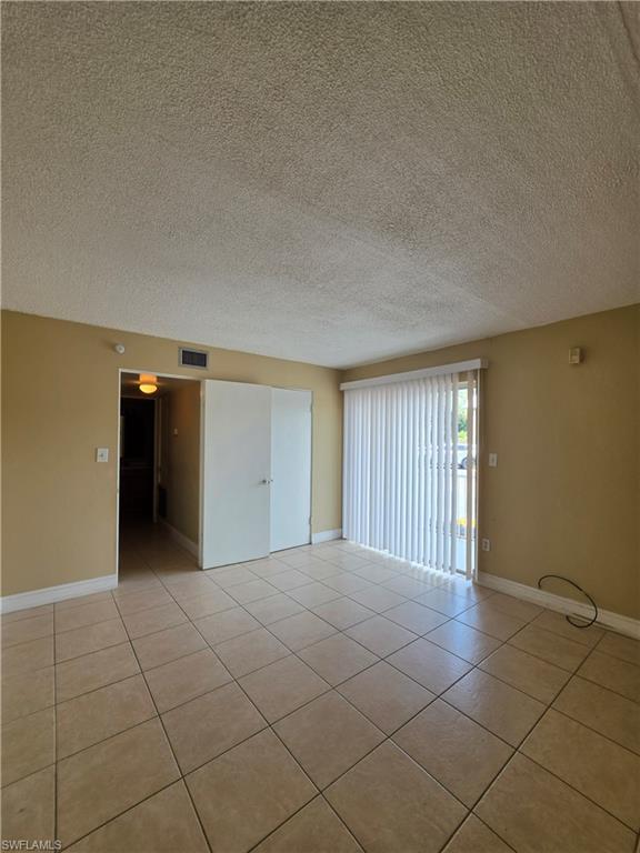 Spacious interior room featuring light-toned tile flooring, light beige wall paint, and white baseboards