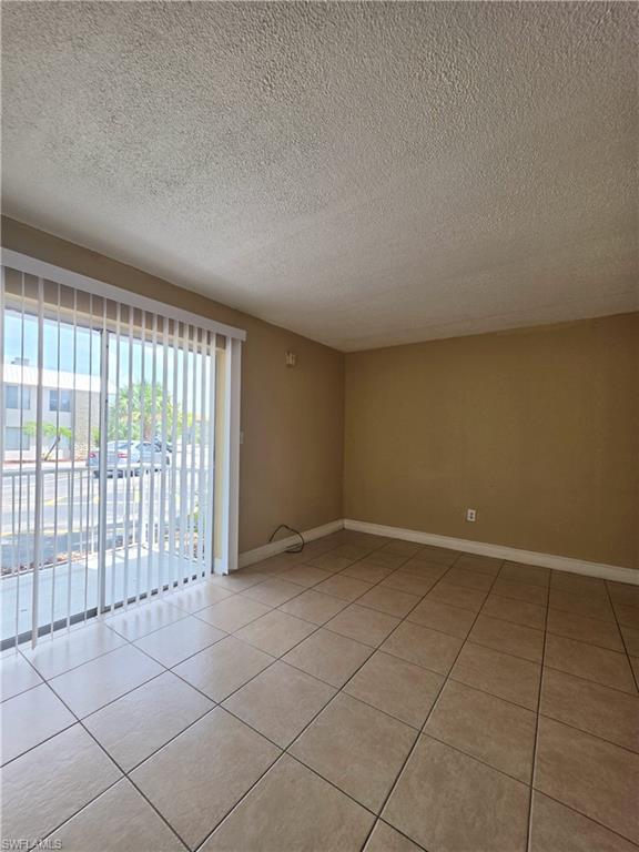 Spacious interior room featuring ceramic tile flooring, neutral wall tones, and a sliding glass door with vertical blinds