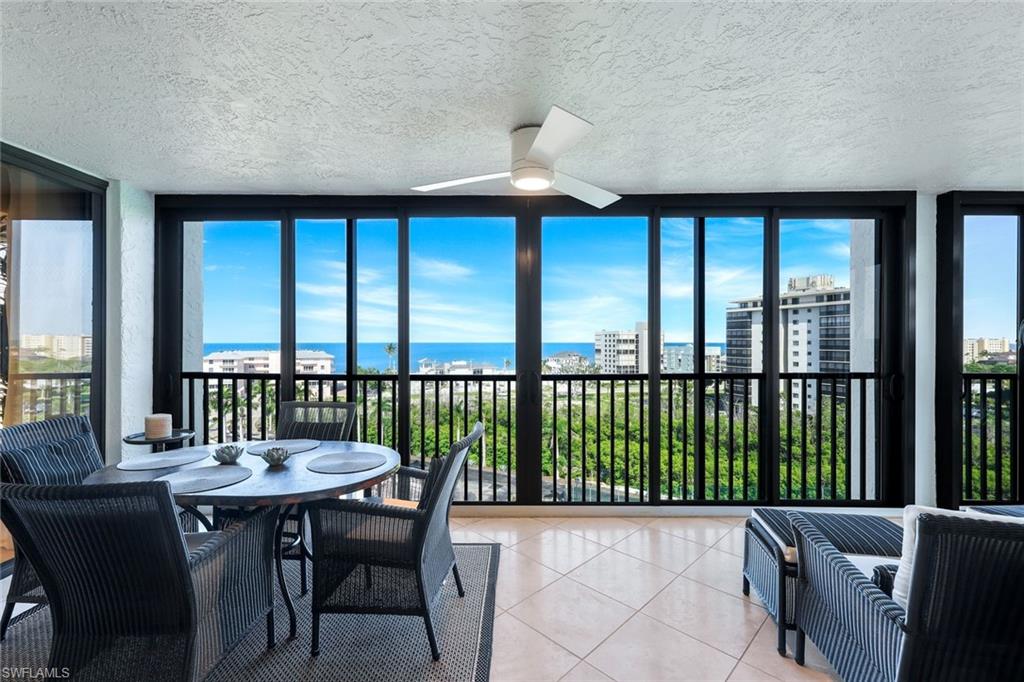 Expansive balcony featuring panoramic water and city views through large windows, a white ceiling fan, and ceramic tile flooring