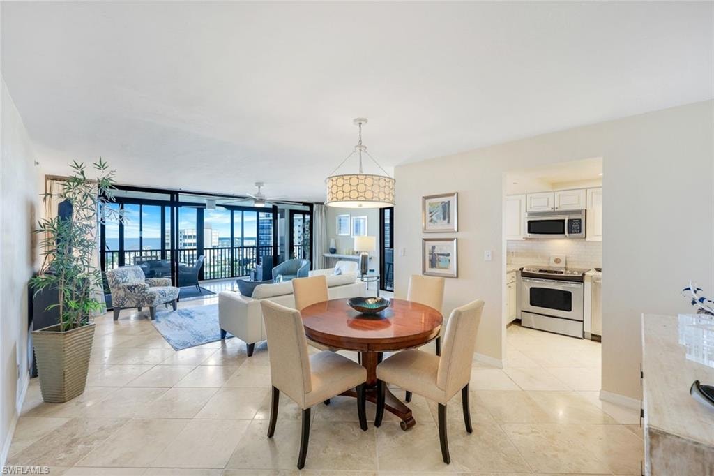 Elegant open-concept living and dining area featuring polished stone flooring, a round wood pedestal dining table with upholstered seating, and a crystal chandelier
