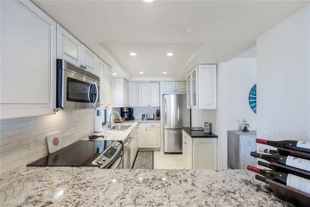 Modern galley kitchen featuring white cabinetry with brushed nickel hardware, stainless steel appliances including a built-in microwave, granite countertops, subway tile backsplash, recessed lighting, and a pass-through opening to the adjacent dining area