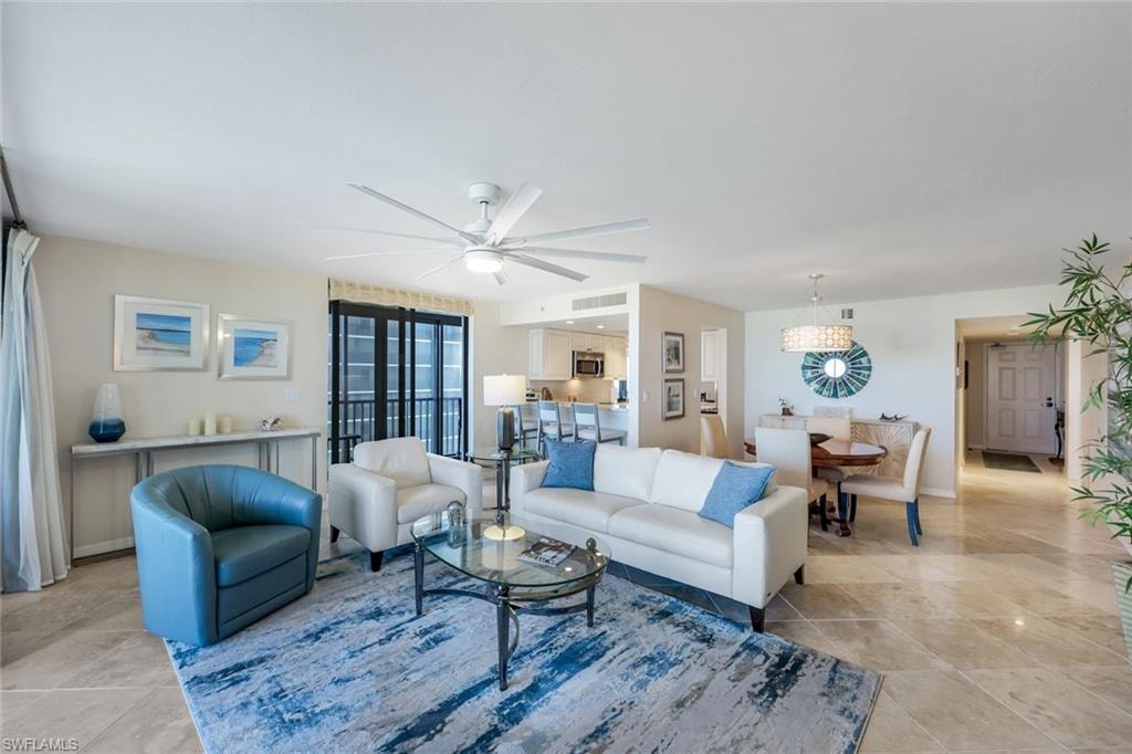 Spacious open-concept living area featuring a wood-finish floor, ceiling fan with integrated lighting, and abundant natural light from multiple glass doors and windows