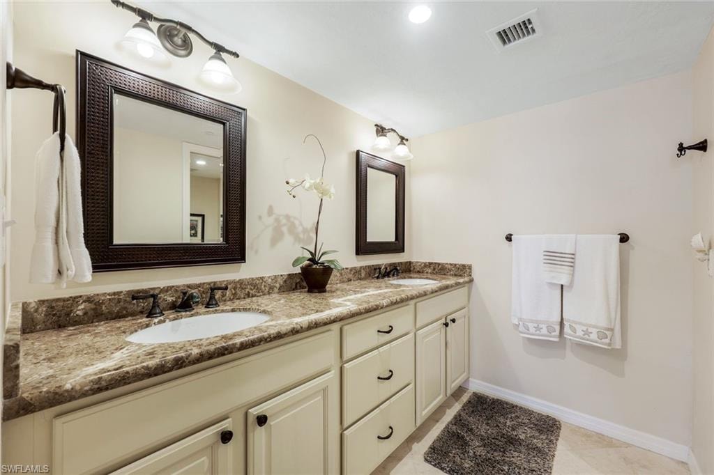 Dual vanity featuring undermount sinks, patterned stone countertops, and cream-colored cabinetry with dark hardware